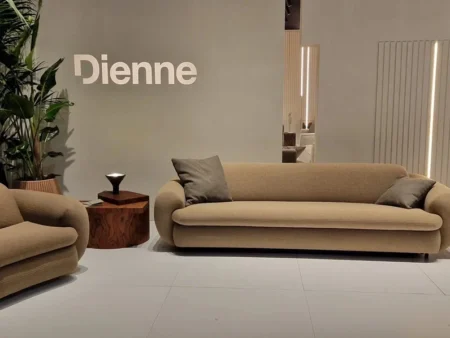 Beige Curvi designsofa og matchende lenestol i strukturvevd tekstil. En moderne sovesofa med memory foam og organisk form, vist i et inspirerende miljø på møbelmesse.
